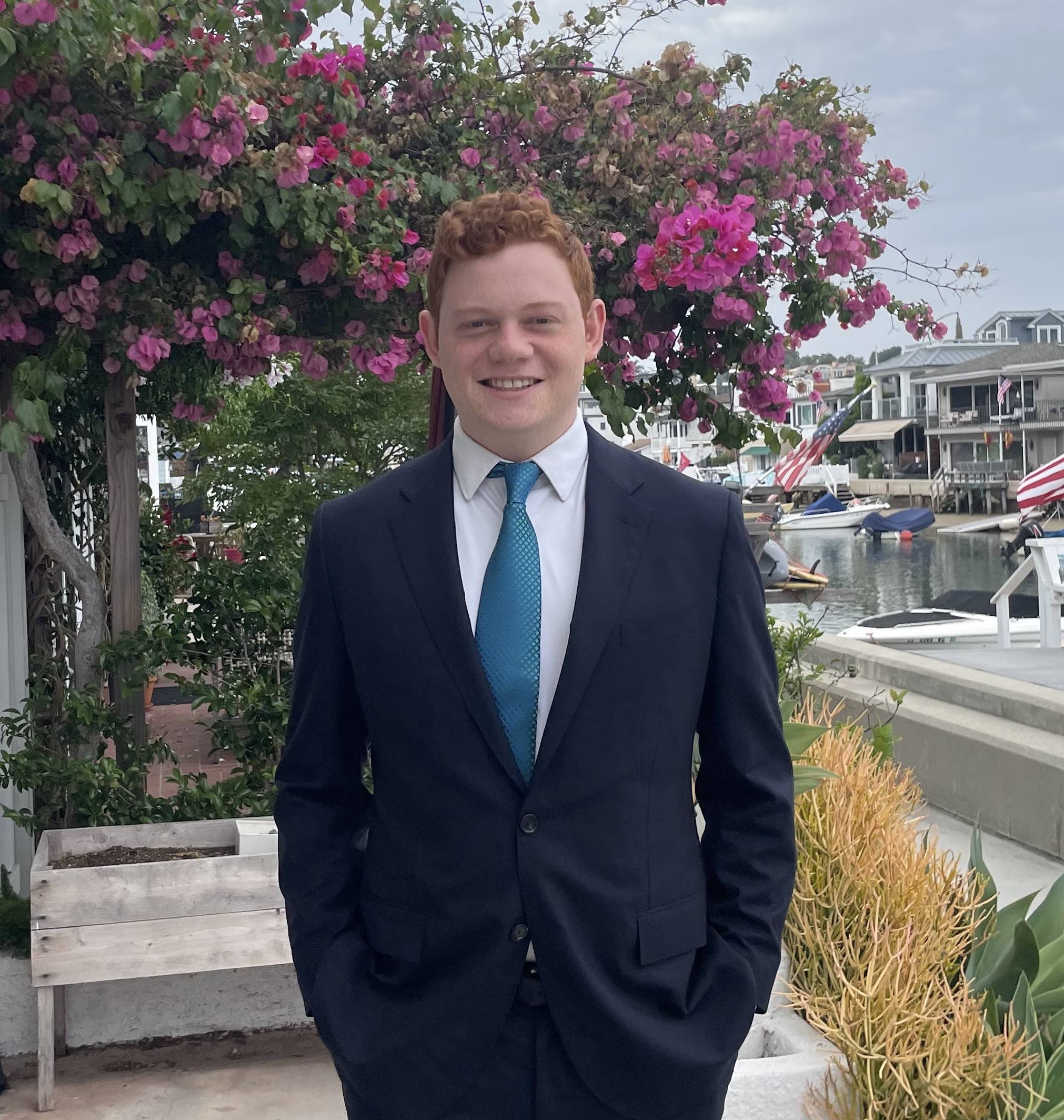 Gilad in a blue suit and tie in front of some pink flowers